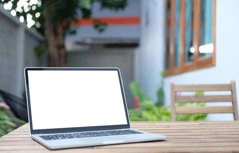 Computer laptop with white empty screen on wooden table at outdoor cafe. Stock Photos