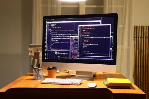 Computer monitor displaying programming code on a wooden desk with coffee and Stock Photos