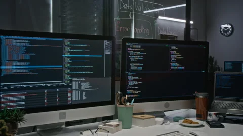 Computer Monitors Displaying Programming Code in Office at Night Stockbeeldmateriaal 348362331
