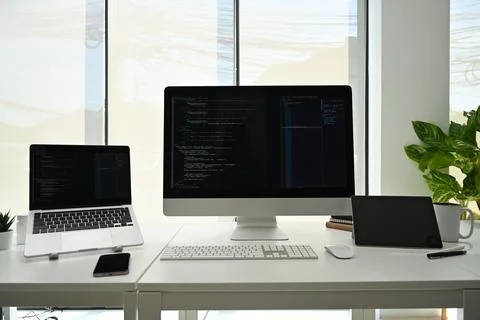 Computer monitors with programming code on white office desk at software 库存照片