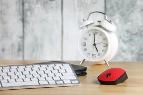 Computer mouse and keyboard on a table. Retro alarm clock. Wooden background. Wo Stock Photos