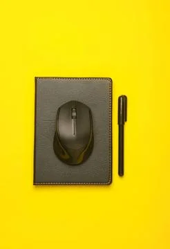 Computer mouse and pen on notebook with yellow background Stockfoto's