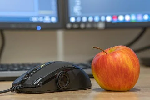 Computer mouse and a red apple on blurred background of light screen. Stock Photos