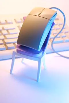 Computer mouse perched on a mini chair, keyboard Foto stock