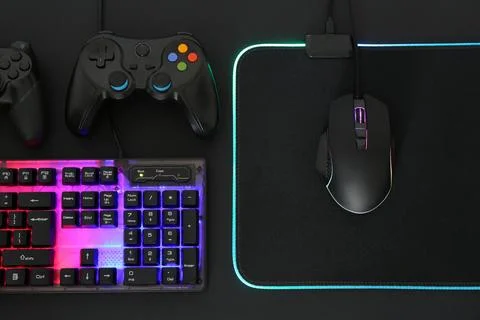 Computer mouse, RGB keyboard and game controllers on black background, flat l Stock Photos
