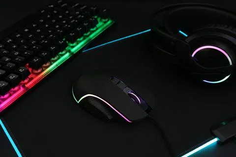 Computer mouse, RGB keyboard and headset on black background, closeup Stock Photos