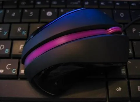 Computer mouse with violet strip laying on black keybord of notebook Stock Photos