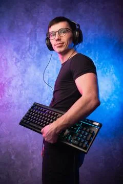 Computer nerd with keyboard over colorful pink and blue neon lit wall Stock Photos