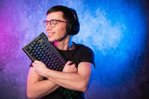 Computer nerd with keyboard over colorful pink and blue neon lit wall Foto stock
