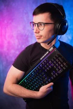 Computer nerd with keyboard over colorful pink and blue neon lit wall Stock Photos