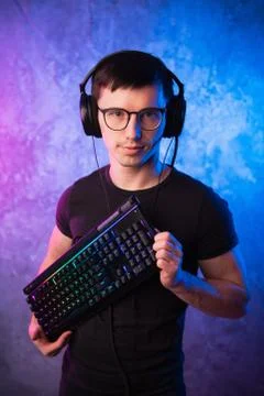 Computer nerd with keyboard over colorful pink and blue neon lit wall Foto stock