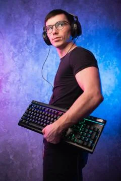Computer nerd with keyboard over colorful pink and blue neon lit wall Stock Photos
