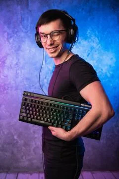 Computer nerd with keyboard over colorful pink and blue neon lit wall Stock Photos