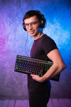 Computer nerd with keyboard over colorful pink and blue neon lit wall Stock Photos