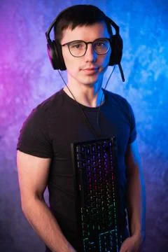 Computer nerd with keyboard over colorful pink and blue neon lit wall Stock Photos