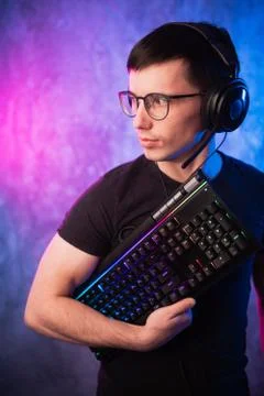 Computer nerd with keyboard over colorful pink and blue neon lit wall Foto stock