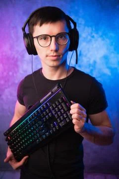 Computer nerd with keyboard over colorful pink and blue neon lit wall Stock Photos