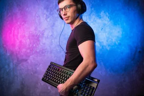 Computer nerd with keyboard over colorful pink and blue neon lit wall Stock Photos