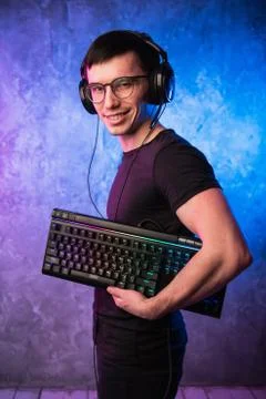 Computer nerd with keyboard over colorful pink and blue neon lit wall Foto stock
