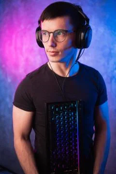 Computer nerd with keyboard over colorful pink and blue neon lit wall Stock Photos