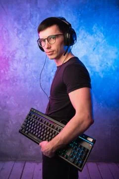 Computer nerd with keyboard over colorful pink and blue neon lit wall Stock Photos
