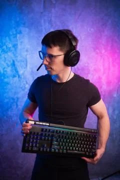 Computer nerd with keyboard over colorful pink and blue neon lit wall Stock Photos
