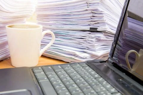 Computer notebook and documents on desk stack up high waiting to be managed 스톡 사진