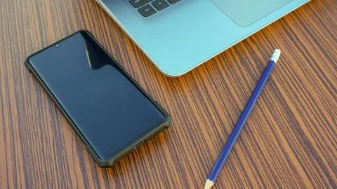 Computer notebook with black smartphone and a blue pencil on a wooden desk. Stock Photos