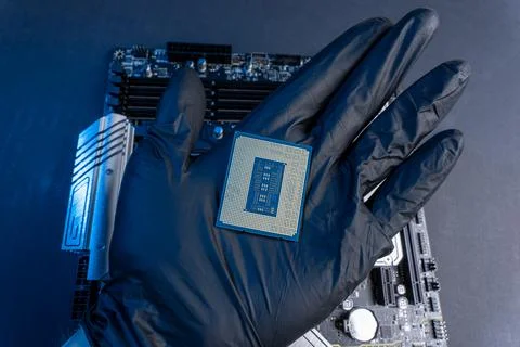 Computer processor in a gloved hand against the background of the motherboard Foto stock