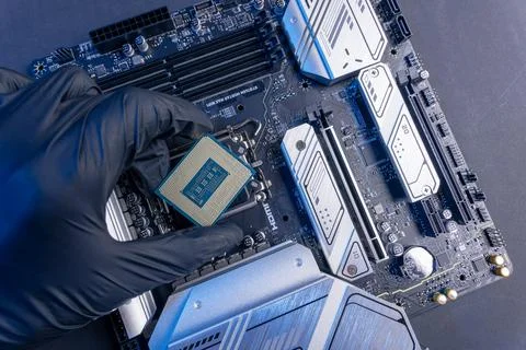 Computer processor in a gloved hand against the background of the motherboard Stock Photos