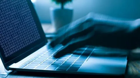 A computer programmer or hacker prints a code on a laptop keyboard to break i Stock Photos