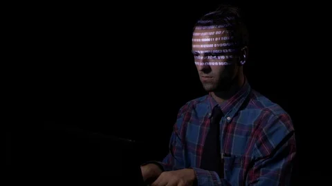 Computer programmer sitting in a dark room and typing while binary code is re Stock Footage 86450027