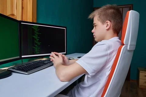 A computer programmer student sits at a computer in his room at a desk on a Stock-Fotos