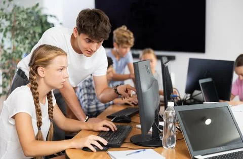 Computer science teacher helps young schoolgirl solve problem on computer Stockfoto's