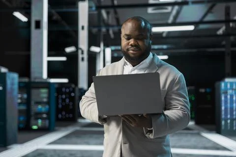 Computer scientist in data center updating systems using laptop, Foto stock