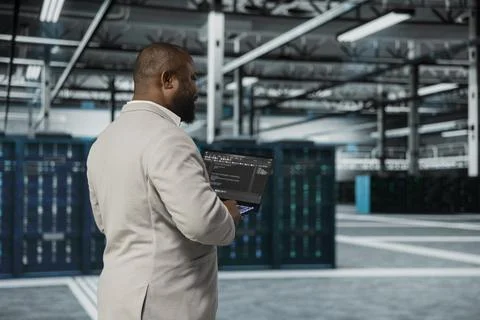 Computer scientist walking in data center running lines of code on laptop Stock Photos