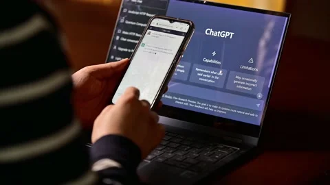 Computer screen with ChatGPT website and person using mobile phone to ask questi Stock Footage 232921995