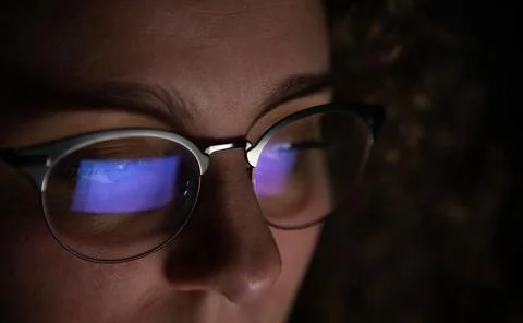 Computer screen reflected in the glasses of a woman who is working at night. Stock Photos