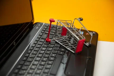 Computer with a small shopping cart lying on a yellow background Stock Photos