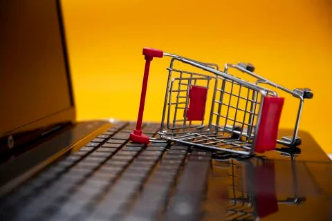 Computer with a small shopping cart lying on a yellow background Stock Photos