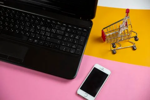 Computer with a small shopping cart lying on a yellow background Stock Photos
