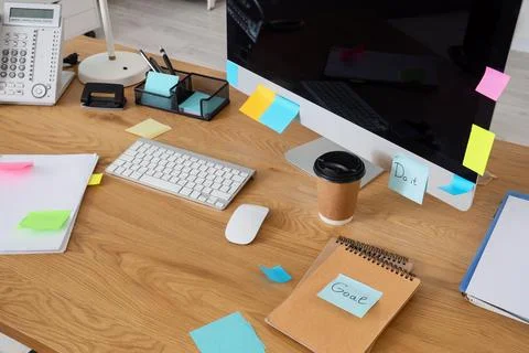 Computer with sticky notes, coffee cup and notebooks on desk in office Stock Photos