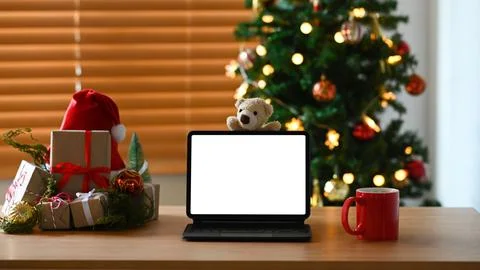 Computer tablet, coffee cup and gift boxes on wooden table near Christmas tree Stock Photos