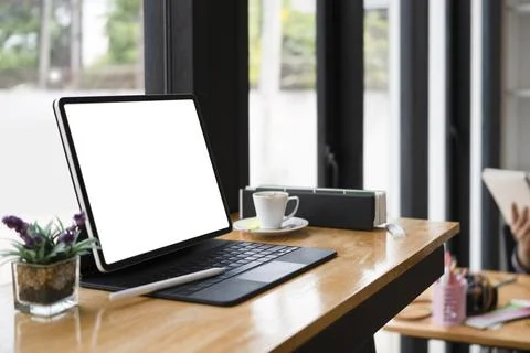 Computer tablet with white screen, coffee cup and book on wooden table. Stock Photos