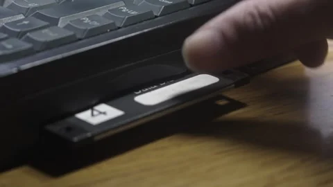 Computer user inserts old tech data storage floppy disc into laptop Stock Footage 312018452