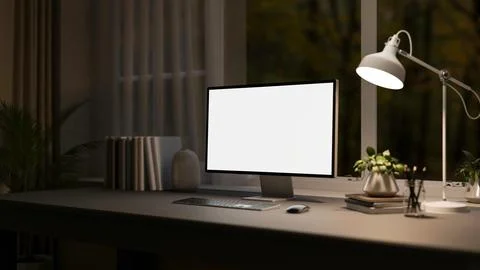 A computer with a white screen mockup sits on a black desk in a dark room a.. Stock Photos