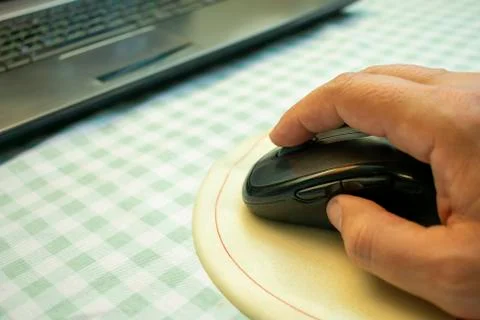 Computer wireless mouse in hand on the rug next to the laptop Stock Photos