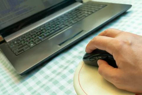Computer wireless mouse in hand on the rug next to the laptop Stock Photos