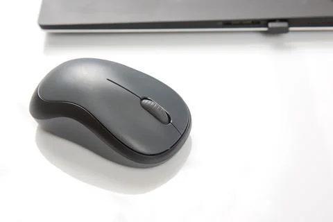 Computer wireless mouse next to a laptop on a white table close-up. electroni Stock Photos