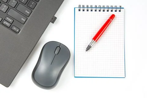 Computer wireless mouse, pen and notepad next to a laptop on a white table .. Stock Photos